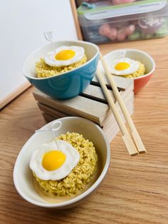 two bowls filled with rice and eggs on top of a wooden table next to chopsticks