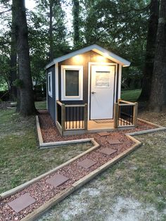 a small shed with steps leading up to the front door and side porch, next to some trees