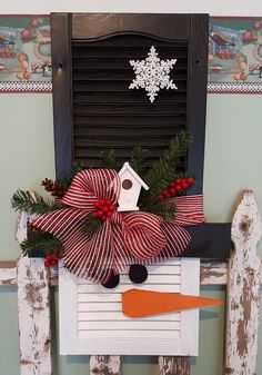 a snowman mailbox decorated with red and white ribbon, pine cones, evergreen leaves and a birdhouse