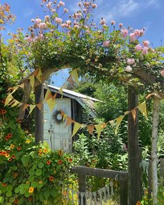 an old shed is surrounded by flowers and greenery with bunting on the door