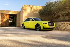 a bright yellow rolls royce parked in front of a stone wall and tree lined driveway