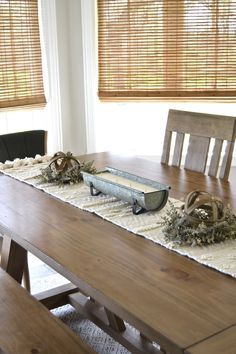 a wooden table topped with a metal tray filled with flowers next to a window covered in blinds