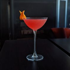 a red cocktail with an orange peel on the rim sitting on a black counter top