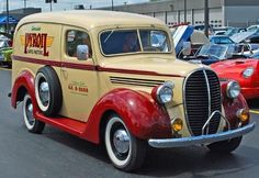 an old yellow and red car is parked in a parking lot next to other cars