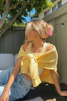 a woman sitting on top of a wooden bench wearing a yellow shirt and blue jeans