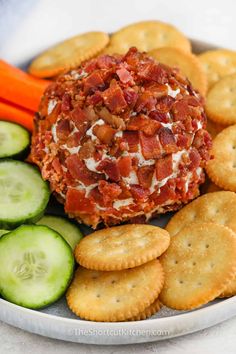 a plate with crackers, cucumbers and cheese ball on it next to carrots