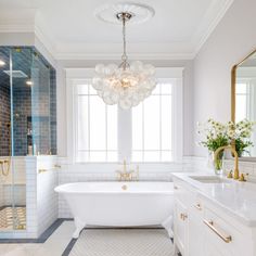 a white bath tub sitting next to a window in a bathroom under a chandelier