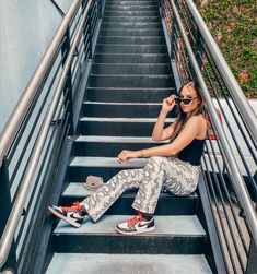 a woman sitting on the stairs talking on her cell phone while wearing camo pants