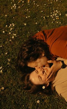 two people laying in the grass with one holding his face to the other's mouth