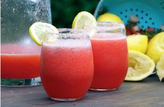 two glasses filled with watermelon juice next to lemons and a pitcher on a table