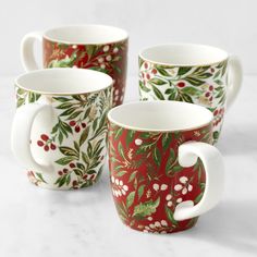 four coffee mugs decorated with red and green holly - berry designs on white background