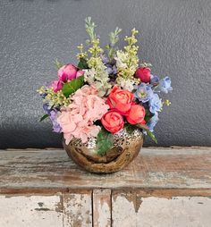 a wooden bowl filled with lots of flowers on top of a table next to a wall