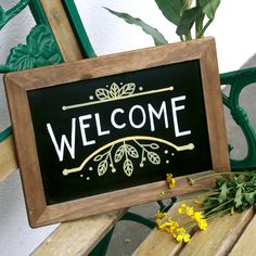 a welcome sign sitting on top of a wooden bench next to a potted plant