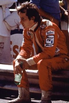 a man in an orange race suit sitting on the side of a boat holding a bottle