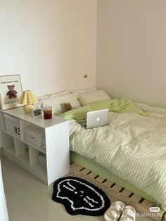 a laptop computer sitting on top of a bed next to a white desk with drawers