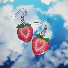 a pair of earrings with a strawberry on them hanging from hooks in front of a cloudy sky