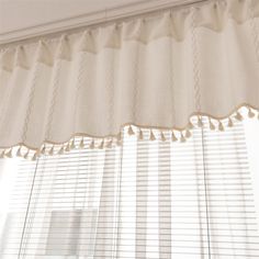 a window with white curtains and tassels hanging from it's valance