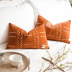 two orange pillows sitting on top of a bed next to a cup and saucer