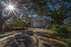 the sun shines brightly in front of a white house with columns and pillars on it