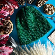 a green knitted hat sitting on top of a blue table next to pine cones