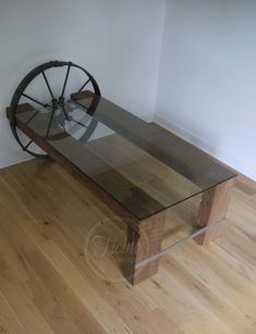 a glass table with a wooden wheel on top in front of a white wall and hardwood floor