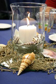 a candle that is sitting in a glass vase with sea shells on the table next to it