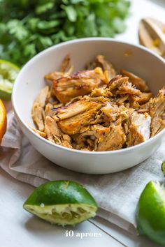 a white bowl filled with shredded meat next to limes