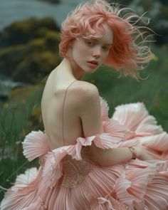 a woman with pink hair is sitting on the grass