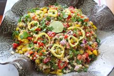 a salad with onions, peppers and cilantro on a silver platter next to a wooden table