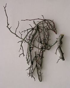 a piece of art made out of branches on a white wall with a bird perched on the branch