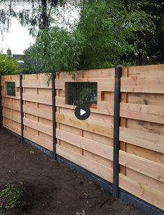 a wooden fence with black metal posts and an animal cage in the center, surrounded by trees