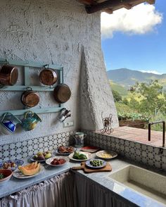 an outdoor kitchen with pots, pans and bowls on the wall next to a sink