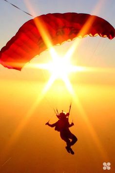 the person is parasailing in the sky at sundown or sunrise, while the sun shines brightly behind them