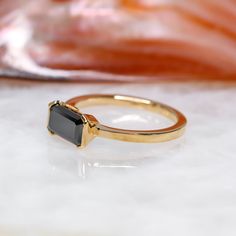 a gold ring with a black stone on it sitting on a white surface next to a bag