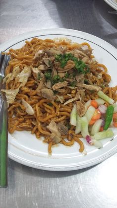 a white plate topped with noodles and veggies on top of a metal table