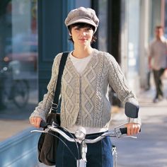 a woman riding a bike down a street next to a sidewalk with people walking on it