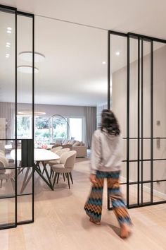 a woman walking through a living room next to a dining room with glass walls and sliding doors