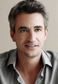 a close up of a person wearing a striped shirt and smiling at the camera with his hands in his pockets