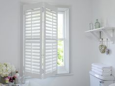 a white bathroom with open shutters on the window