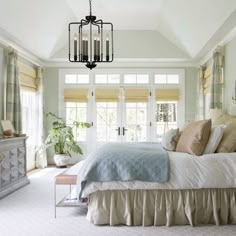 a large bed sitting under a chandelier in a bedroom next to two windows