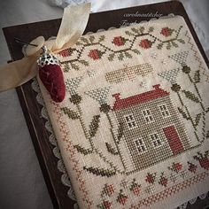 a cross stitch sample with a red house on it and a ribbon around the edge