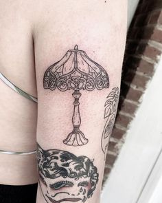 a woman's arm with tattoos on it and a lamp in the corner behind her