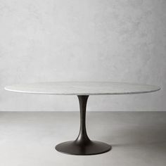 an oval white marble dining table with black metal base and round, circular shaped top