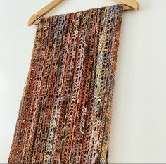 a multicolored crocheted scarf hanging on a wooden hanger against a white wall