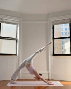 a woman is doing yoga on a mat in front of two windows with no curtains