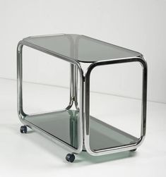 a chrome and glass side table with wheels on the bottom, sitting on a white surface