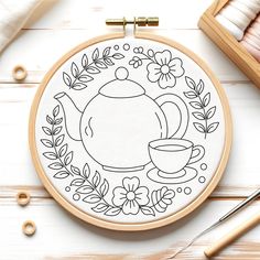 an embroidery pattern with a teapot and cup on it, surrounded by other crafting supplies