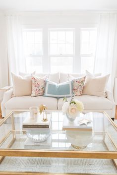 a living room filled with furniture and flowers on top of a glass table in front of a window