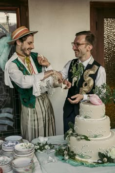 two men standing next to each other in front of a cake on top of a table