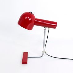 a red desk lamp sitting on top of a white table next to a red object